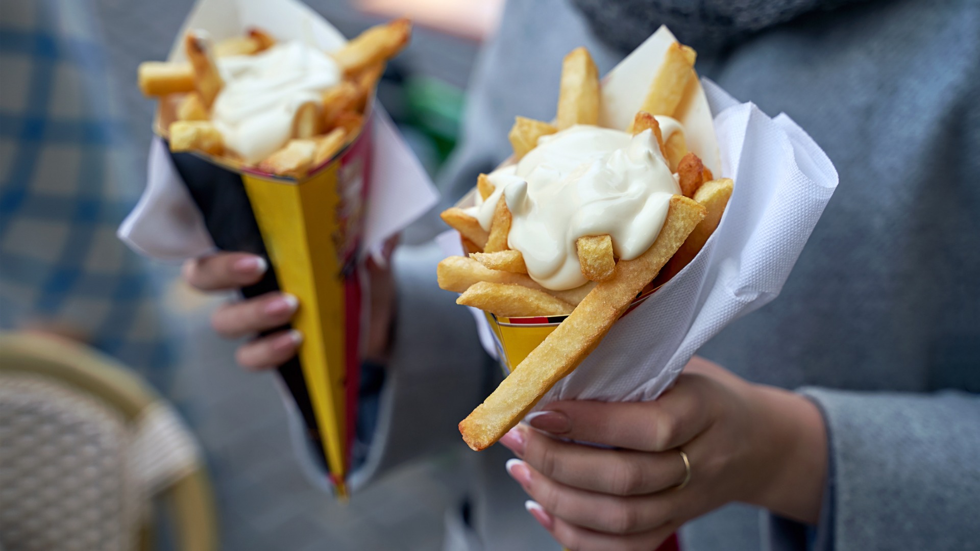 This image is a close-up of a woman holding two paper cones filled with Belgian frites, topped with mayonnaise sauce. Sampling Belgian frites is one of the main reasons to visit Brussels.